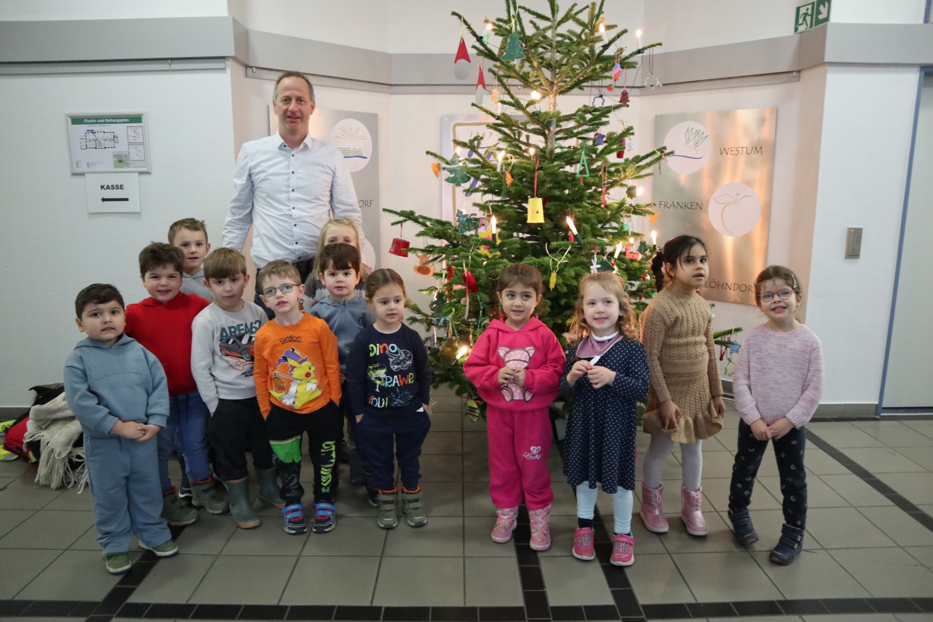 Das Foto zeig die Kita-Kinder und den Büroleiter vor dem geschmückten Weihnachtsbaum.