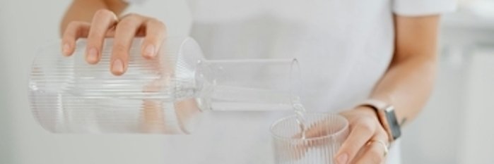 Trinkwasser Das Foto zeigt eine Person, die Trinkwasser in ein Glas gießt.